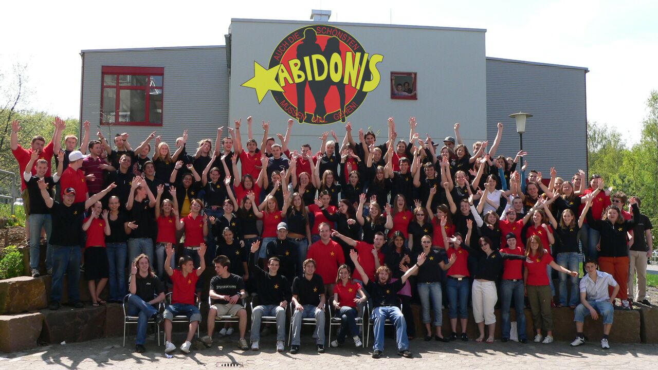 Gruppenfoto des Abiturjahrgangs 2006 vor dem ABIDONIS-Logo an der Wand der Theo-Koch-Schule